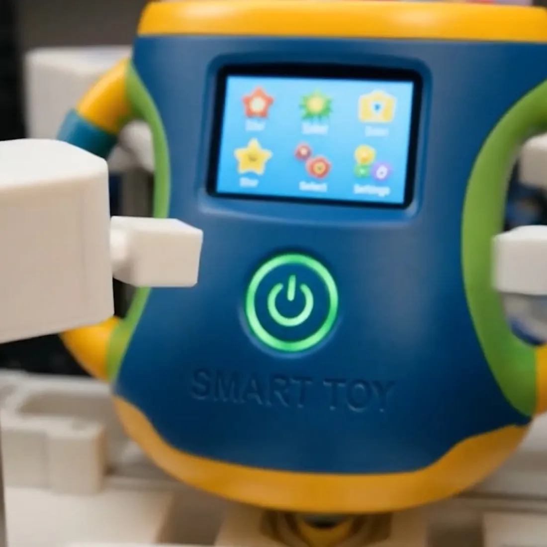 A consumer smart toy held by white robotic grippers inside the test enclosure